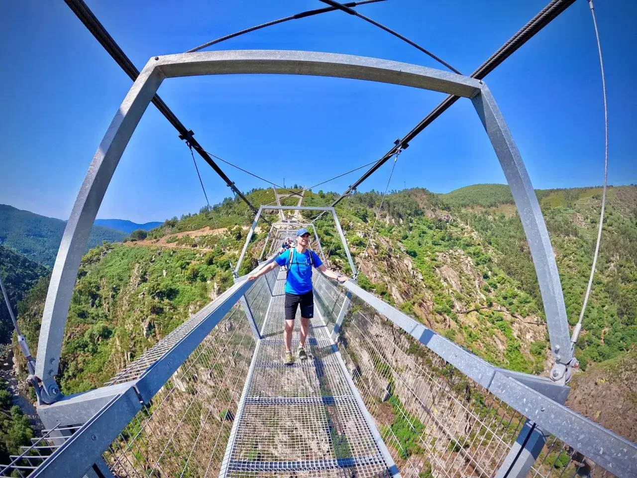 Hombre en el puente Arouca, una pasarela peatonal suspendida sobre un profundo cañón verde.