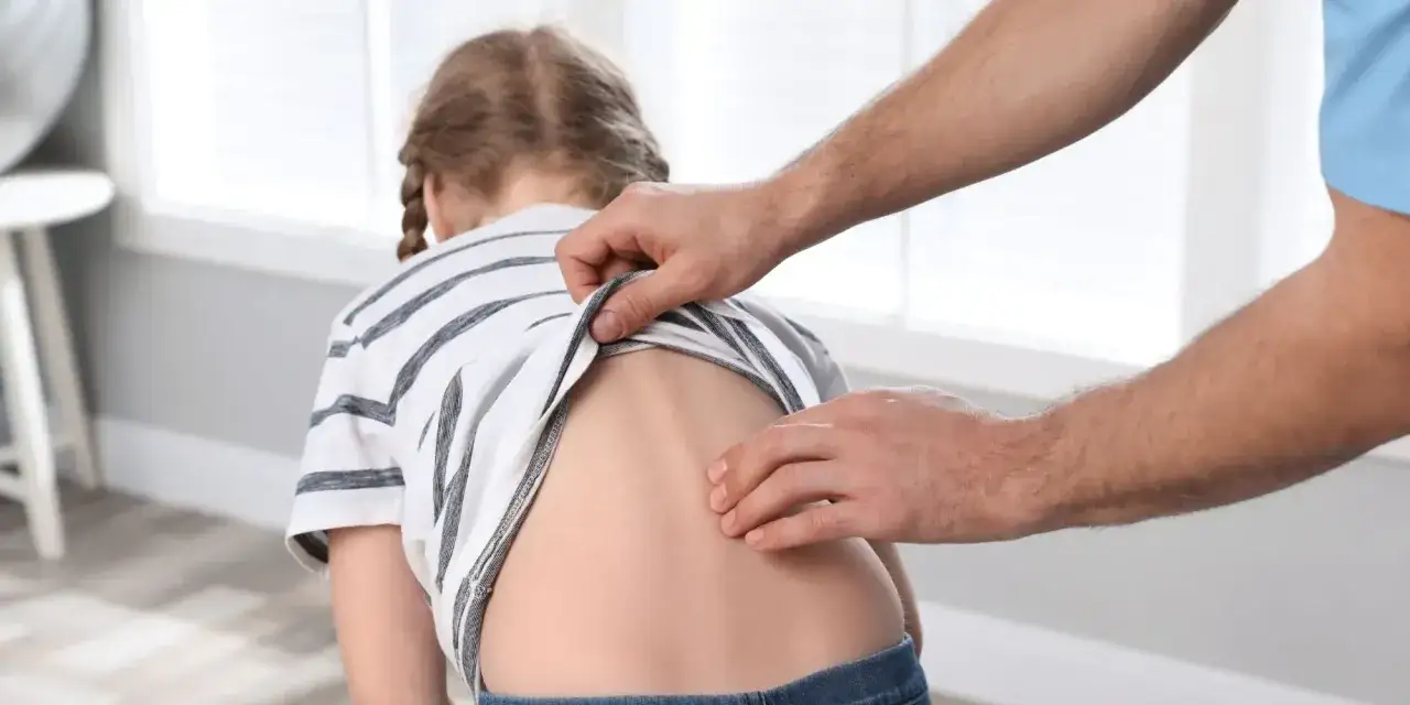Fizjoterapeuta bada plecy dziecka, sprawdzając lordozę lędźwiową.