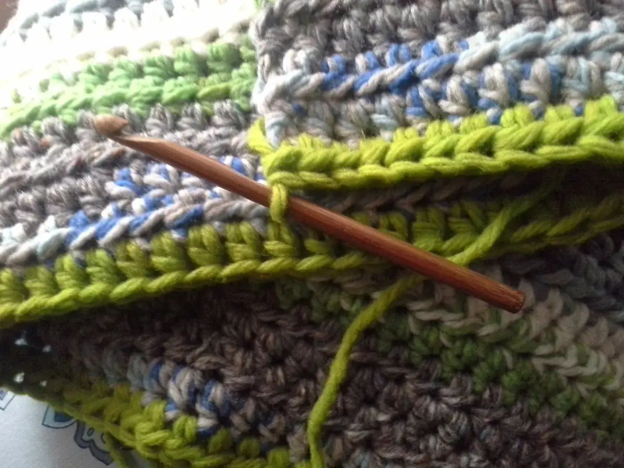 Coperta ai ferri con avanzi di lana, un'opera in corso con colori vivaci e un uncinetto di legno.