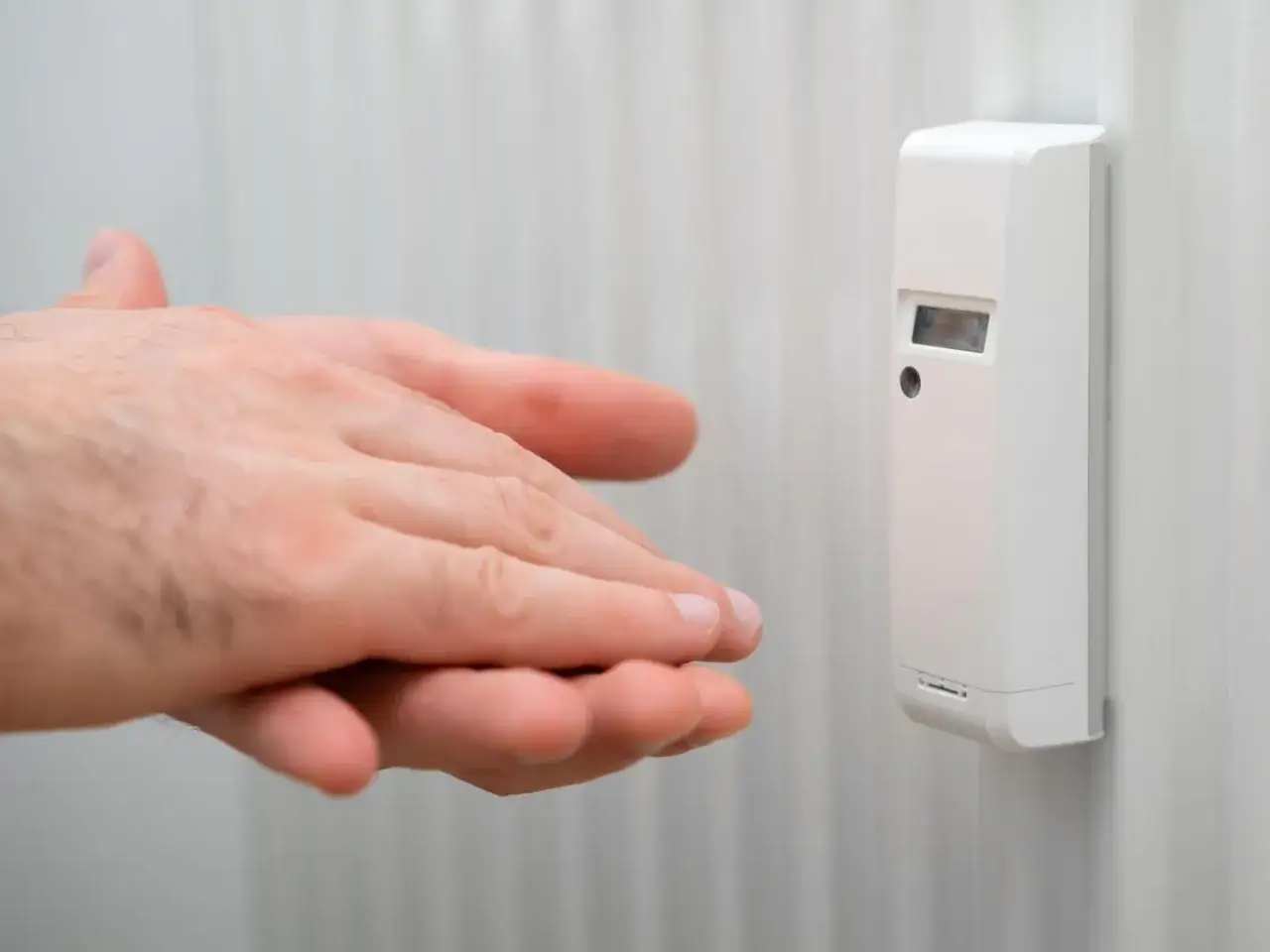 Mani vicine a un ripartitore di calore su un termosifone, per misurare la temperatura.