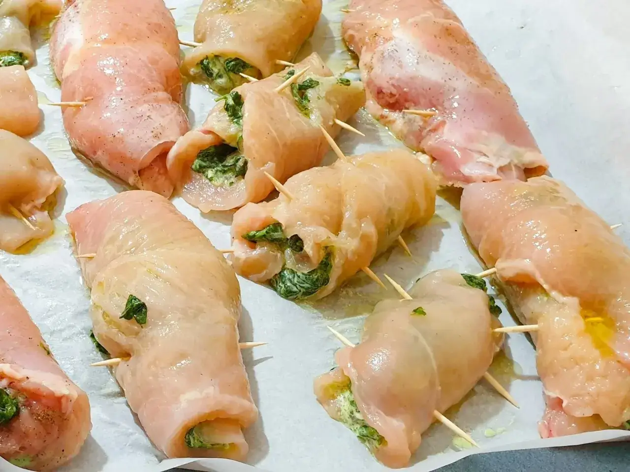 Szybkie danie z fileta z kurczaka: roladki z nadzieniem szpinakowym, zabezpieczone wykałaczkami, gotowe do pieczenia.