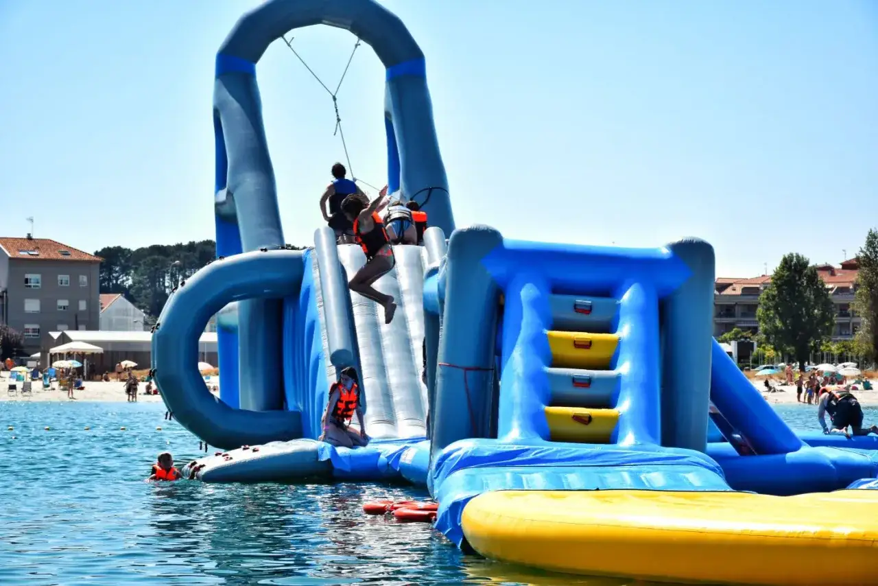 Niños disfrutan en un divertido parque acuático en Cantabria. Una chica salta de un tobogán inflable azul.
