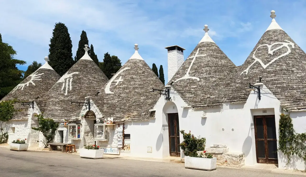 Ecco cosa sono i trulli: case coniche in pietra tipiche della Puglia, con tetti decorati da simboli bianchi.