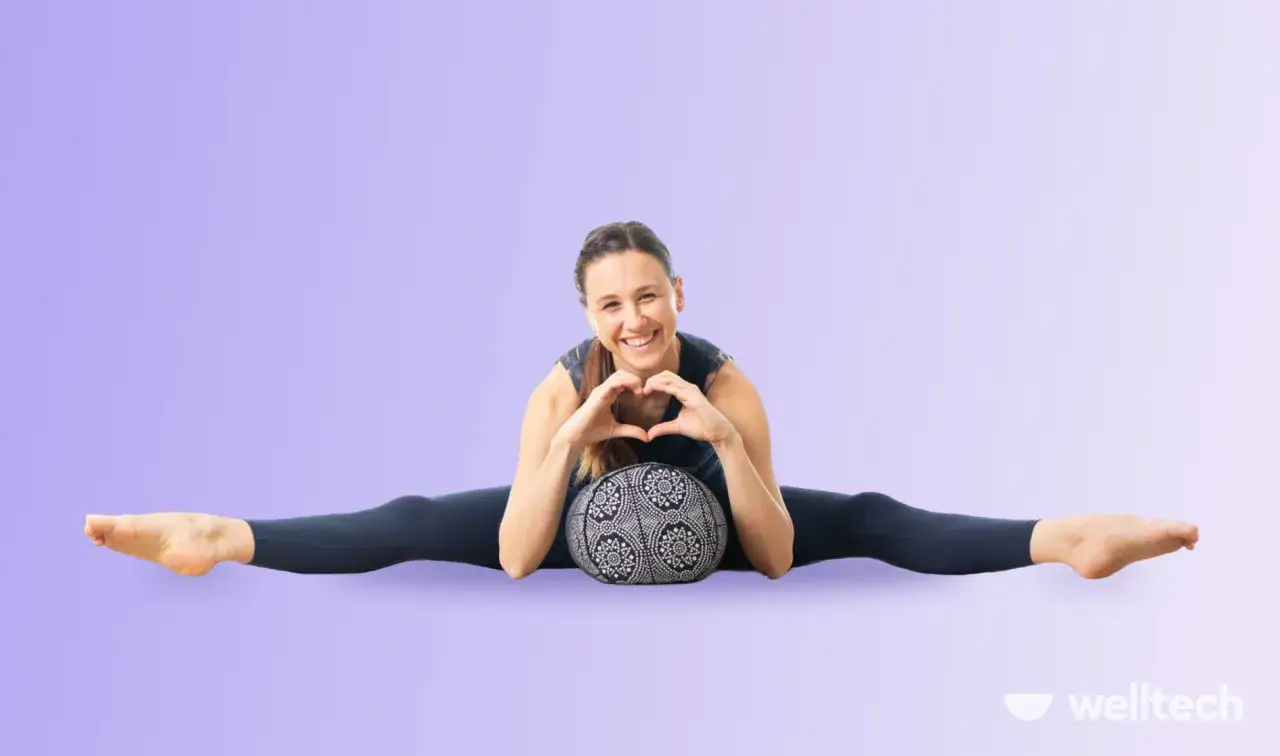 Uśmiechnięta kobieta w pozycji supta baddha konasana z poduszką, tworzy serce dłońmi.