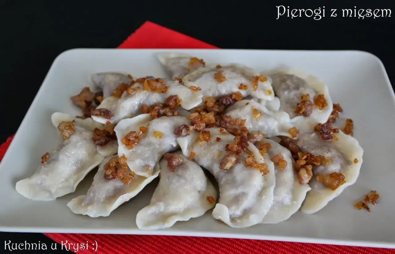 Pyszne pierogi z mięsem, polane skwarkami, ułożone na białym talerzu.