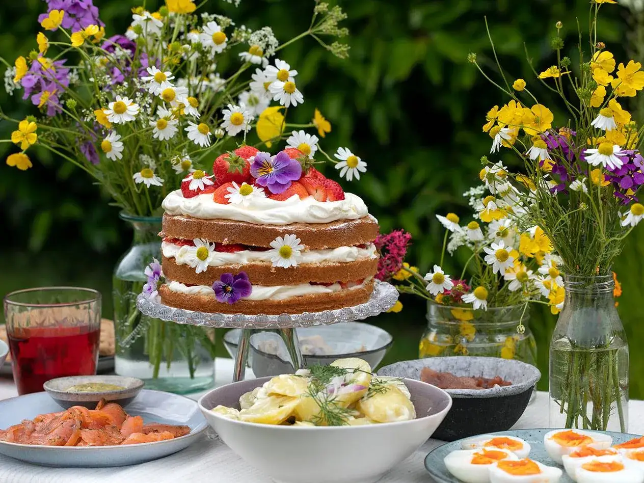 En vacker midsommar dukning med jordgubbst&aring;rta, sill, potatissallad och blommor.