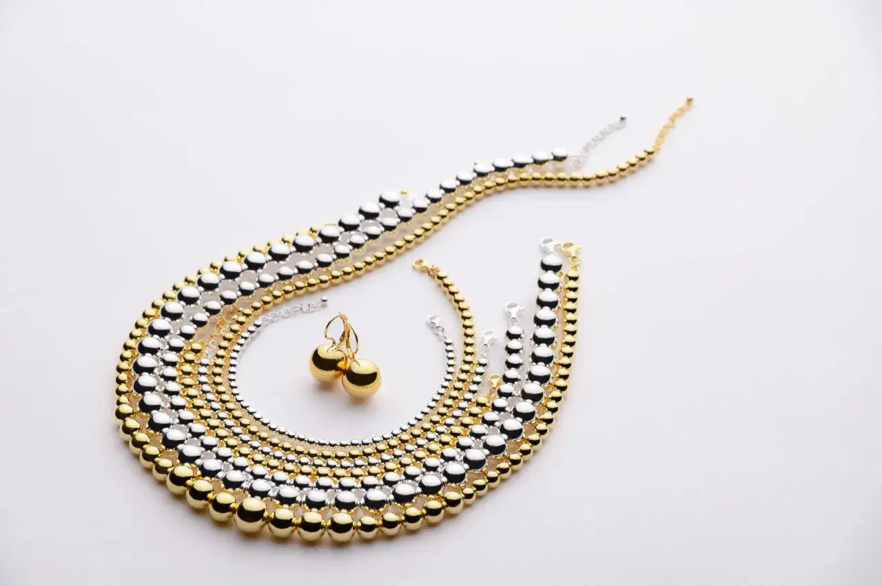 Still life di gioielli: collane e bracciali a palline alternate oro e argento, con orecchini pendenti.