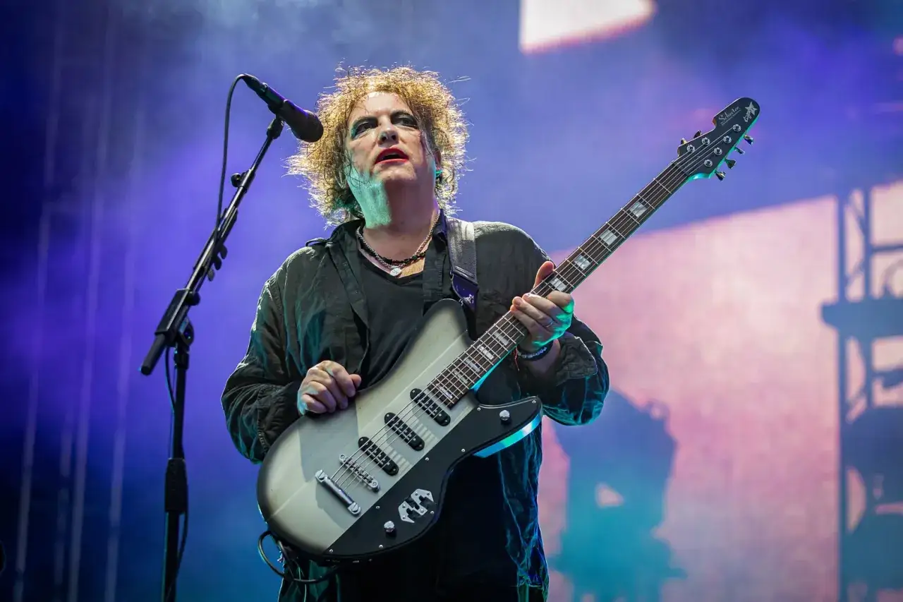 Robert Smith z The Cure gra na gitarze podczas koncertu, tworząc niepowtarzalną atmosferę muzyki zespołu.
