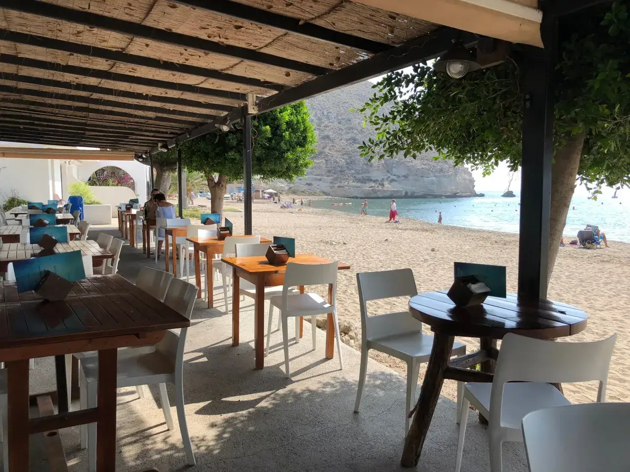 Mesas y sillas en un **restaurante agua amarga** con vista a la playa y al mar.