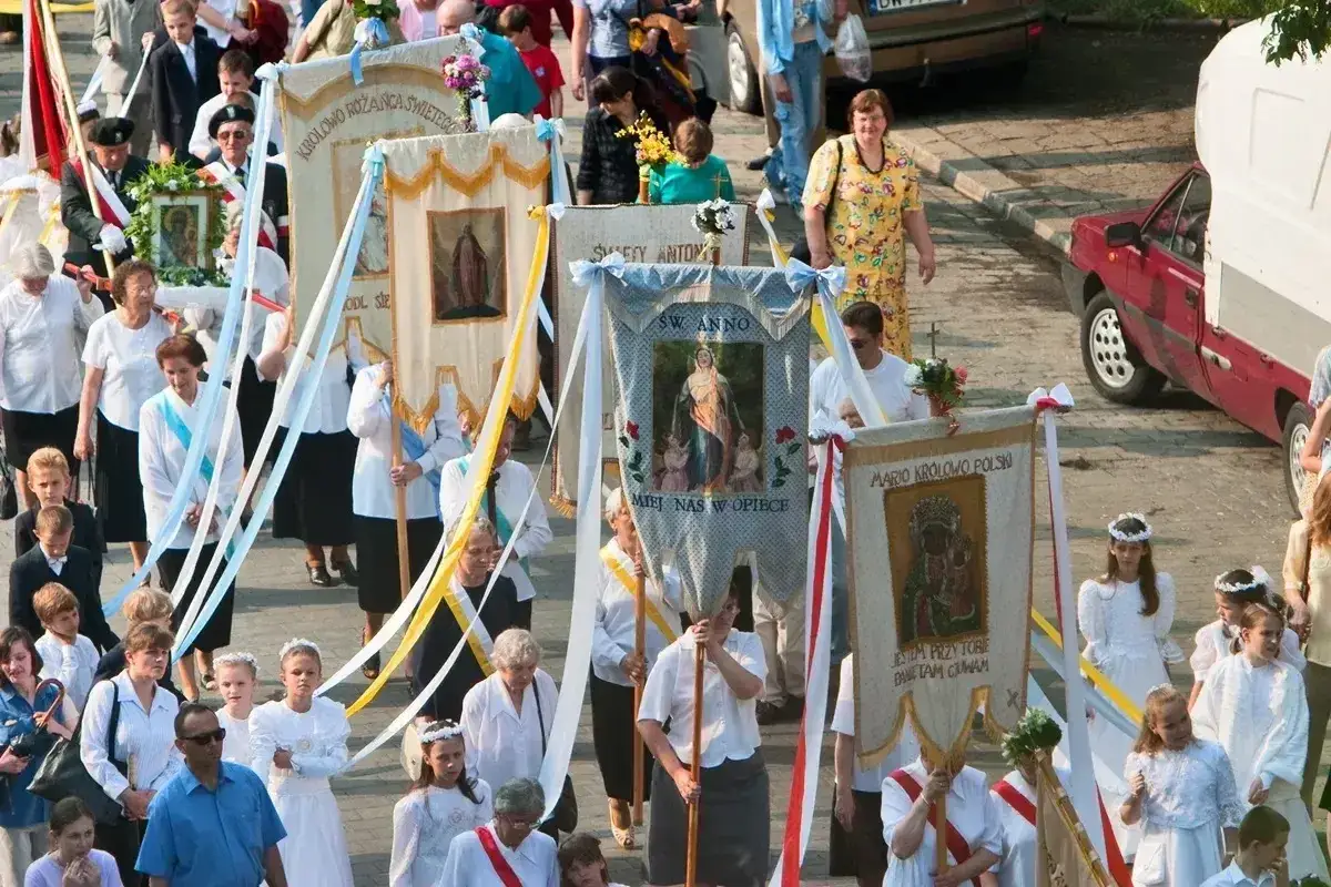 Procesja z chorągwiami religijnymi. Czy Boże Ciało jest dniem wolnym od pracy? Widać ludzi w strojach odświętnych, dzieci w bieli.