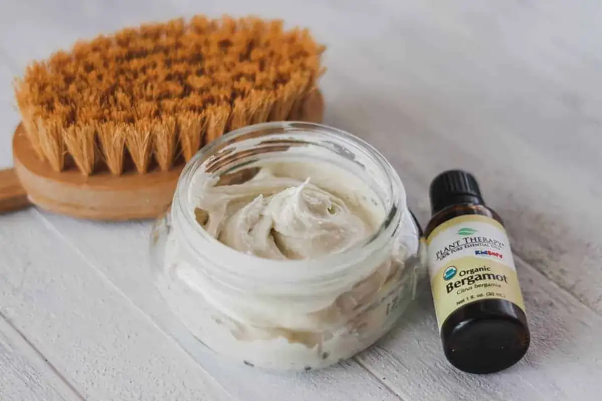 Creme f&uuml;r Hitzeschutz selber machen: eine B&uuml;rste, eine Sch&uuml;ssel mit selbstgemachter Creme und eine Flasche Bergamotte&ouml;l.