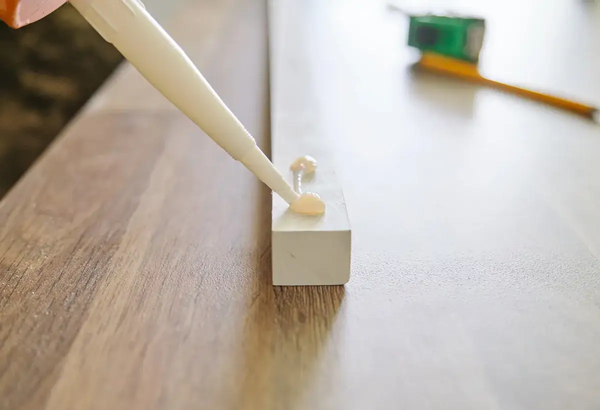 Application de colle pour fixer deux meubles entre eux sans percer. Un tube de colle d&eacute;pose des gouttes sur une pi&egrave;ce de bois.