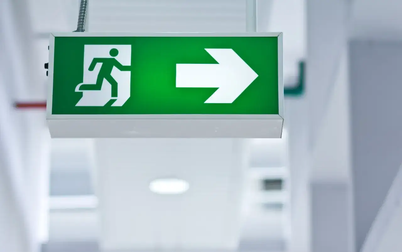 Panneau de sortie de secours vert lumineux avec une silhouette courant vers une fl&egrave;che. Le **baes signification** est clair : une voie d'&eacute;vacuation.
