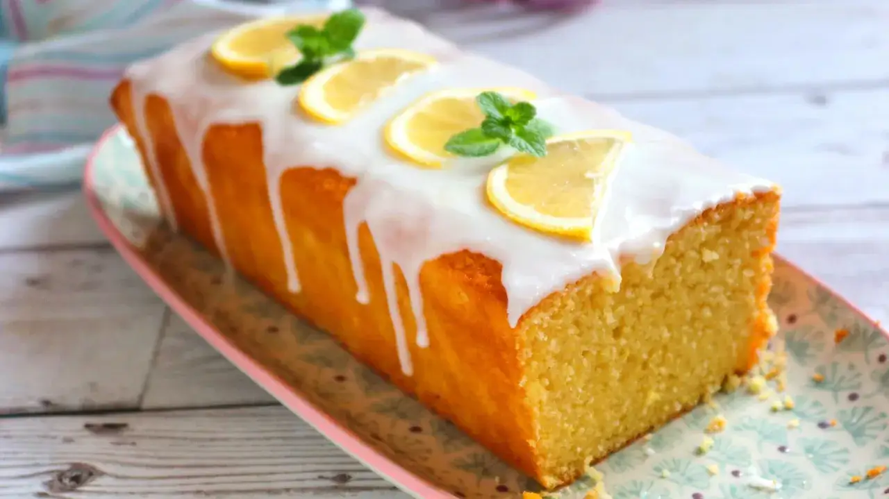Delicioso pastel de limón cubierto con glaseado blanco y decorado con rodajas de limón y hojas de menta.