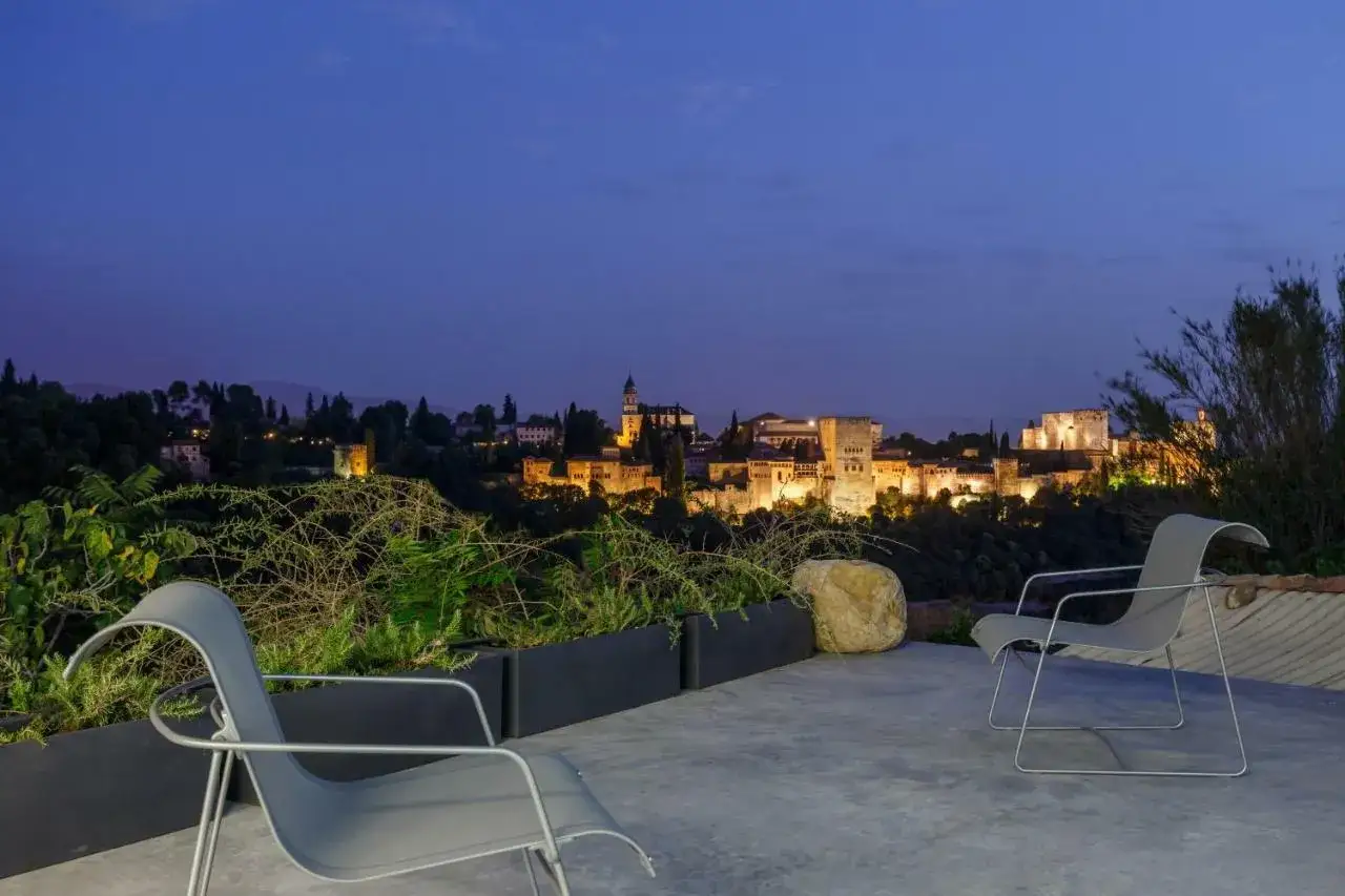 Dos sillas modernas en una terraza con vistas a las iluminadas casas de lujo en Granada al anochecer.