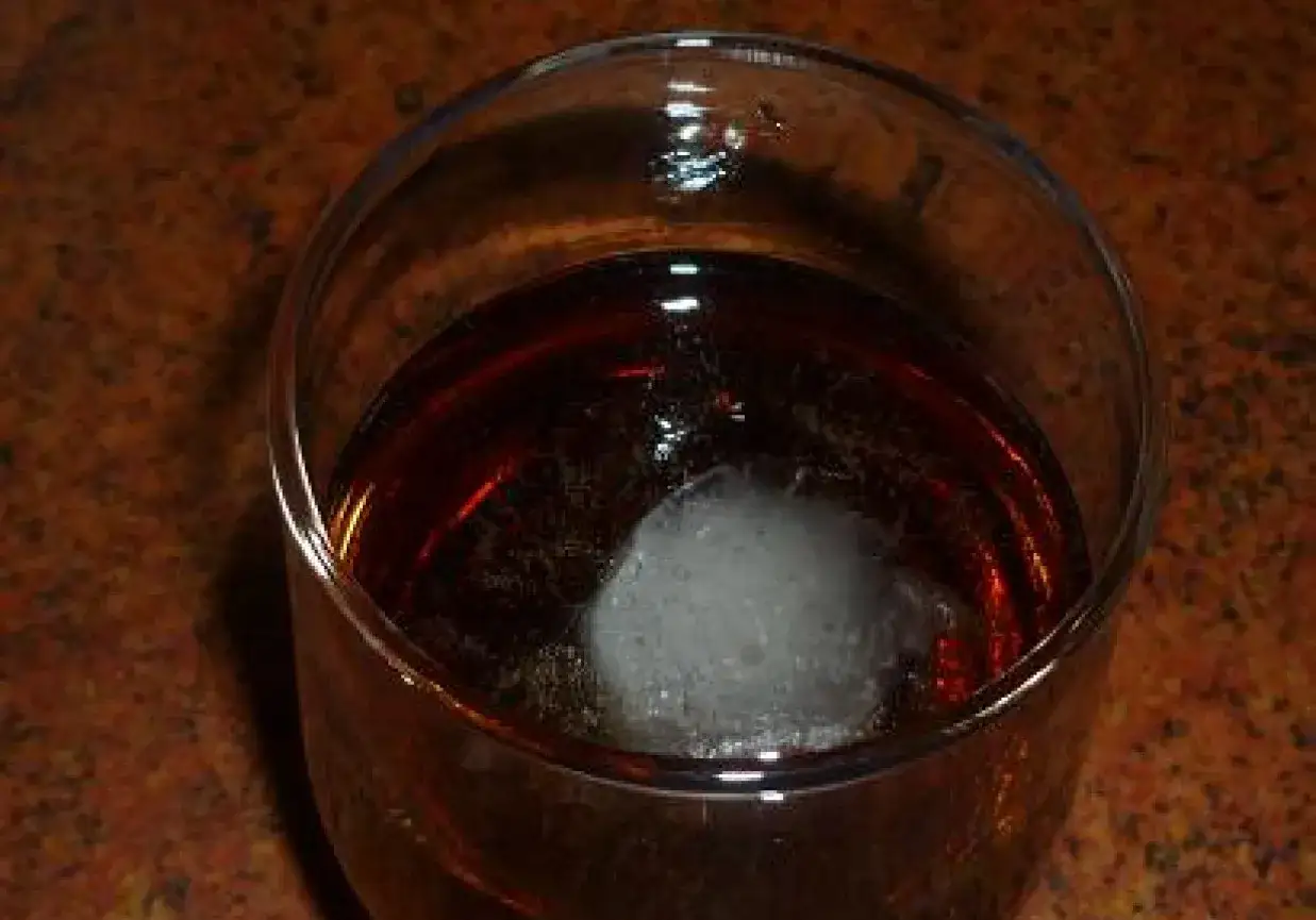 Szklanka z ciemnym napojem i kostką lodu. Idealny drink na upalny dzień: metaxa z colą.