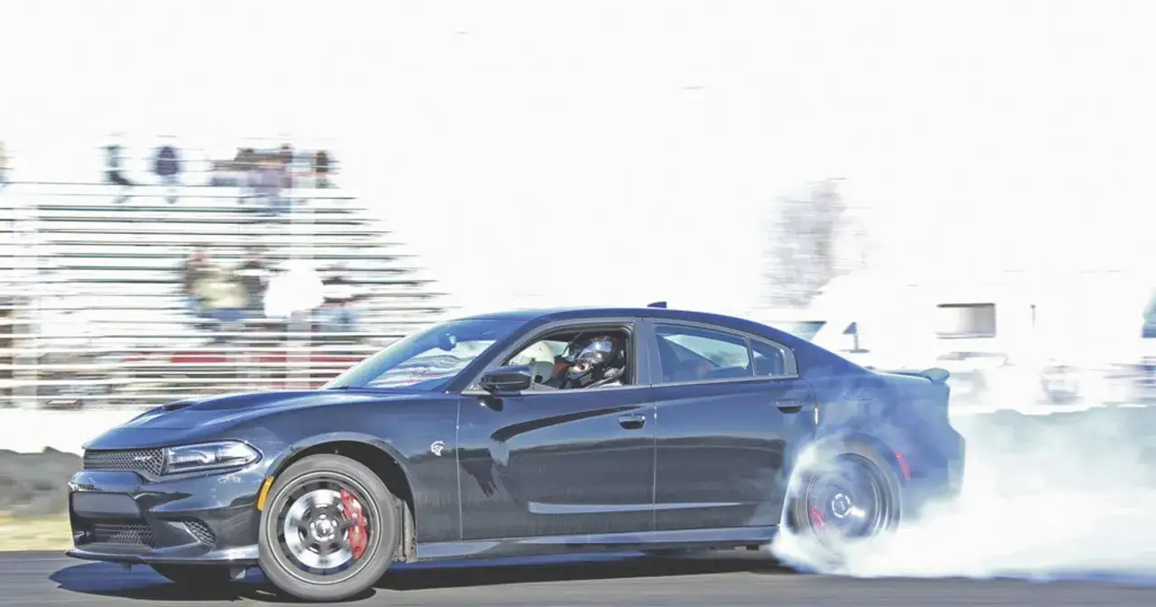 Czarny Charger Hellcat z kierowcą w kasku wykonuje drift, zostawiając za sobą chmurę dymu.