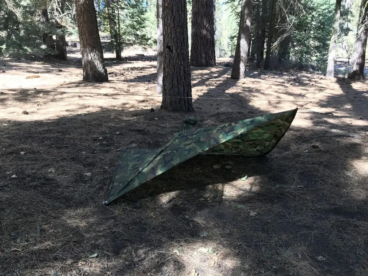 Un poncho de supervivencia camuflado se extiende en un bosque, listo para protegerte.