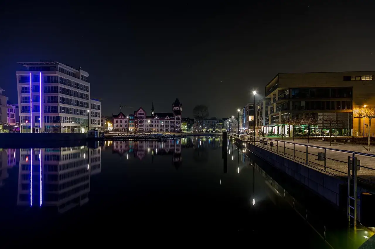 Moderne und historische Geb&auml;ude spiegeln sich im ruhigen Wasser. Dortmund bei Nacht, ein malerischer Anblick mit Lichtern, die die Dunkelheit durchbrechen.