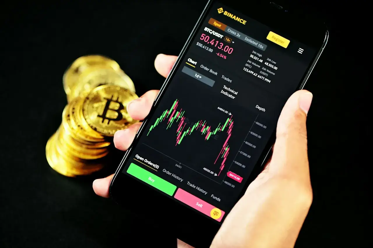 Ręka trzyma smartfon z wykresem kursu Bitcoina na Binance. Zastanawiasz się, czy Binance czy Zonda to lepszy wyb&oacute;r?