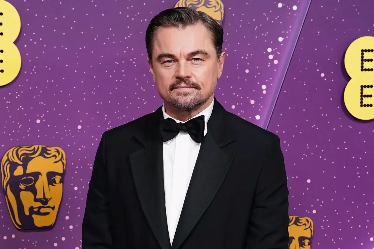 Leonardo DiCaprio w smokingu, z brodą i muszką, na fioletowym tle z gwiazdkami i logotypami. Czekał na swojego Oscara.
