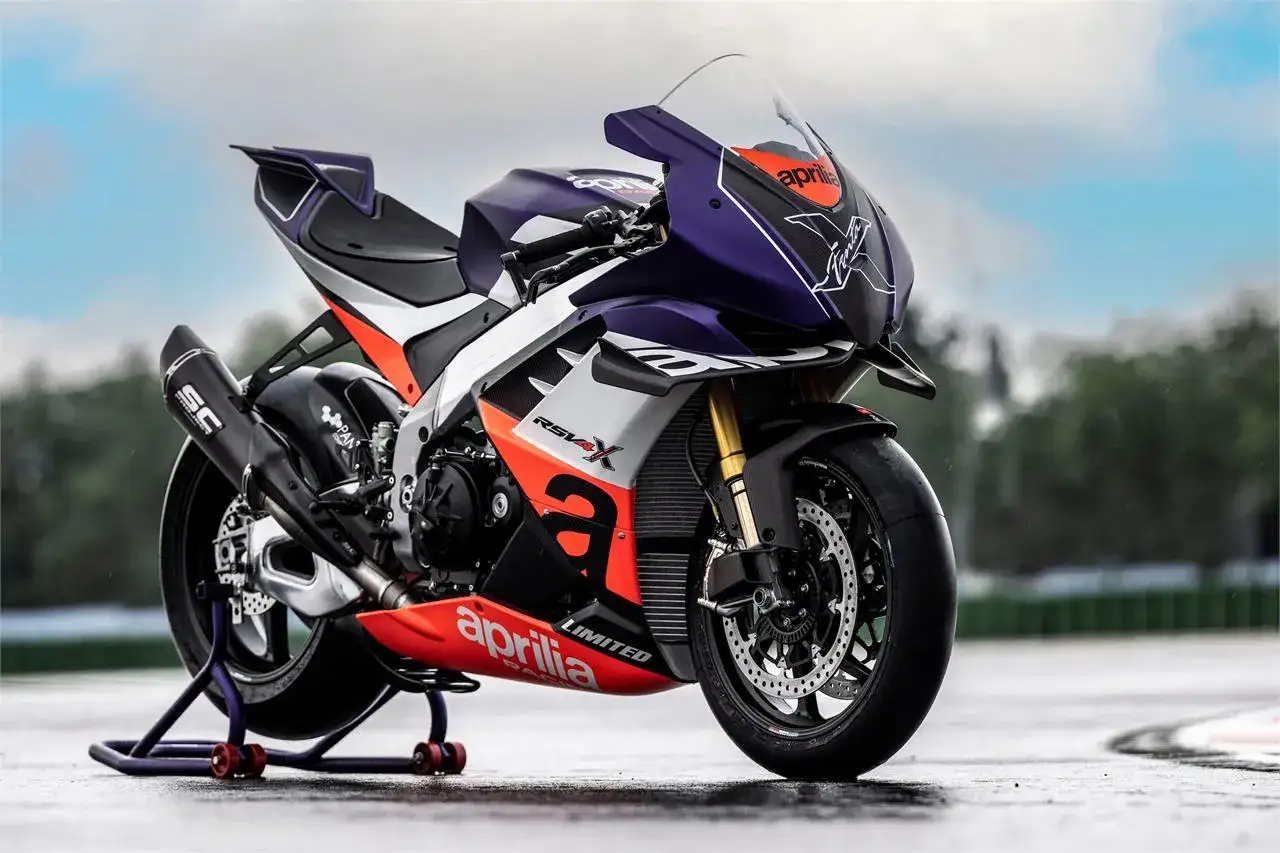 La Aprilia RSV4 1100, una bestia de circuito con carenado morado y detalles en naranja, lista para la acción en pista mojada.