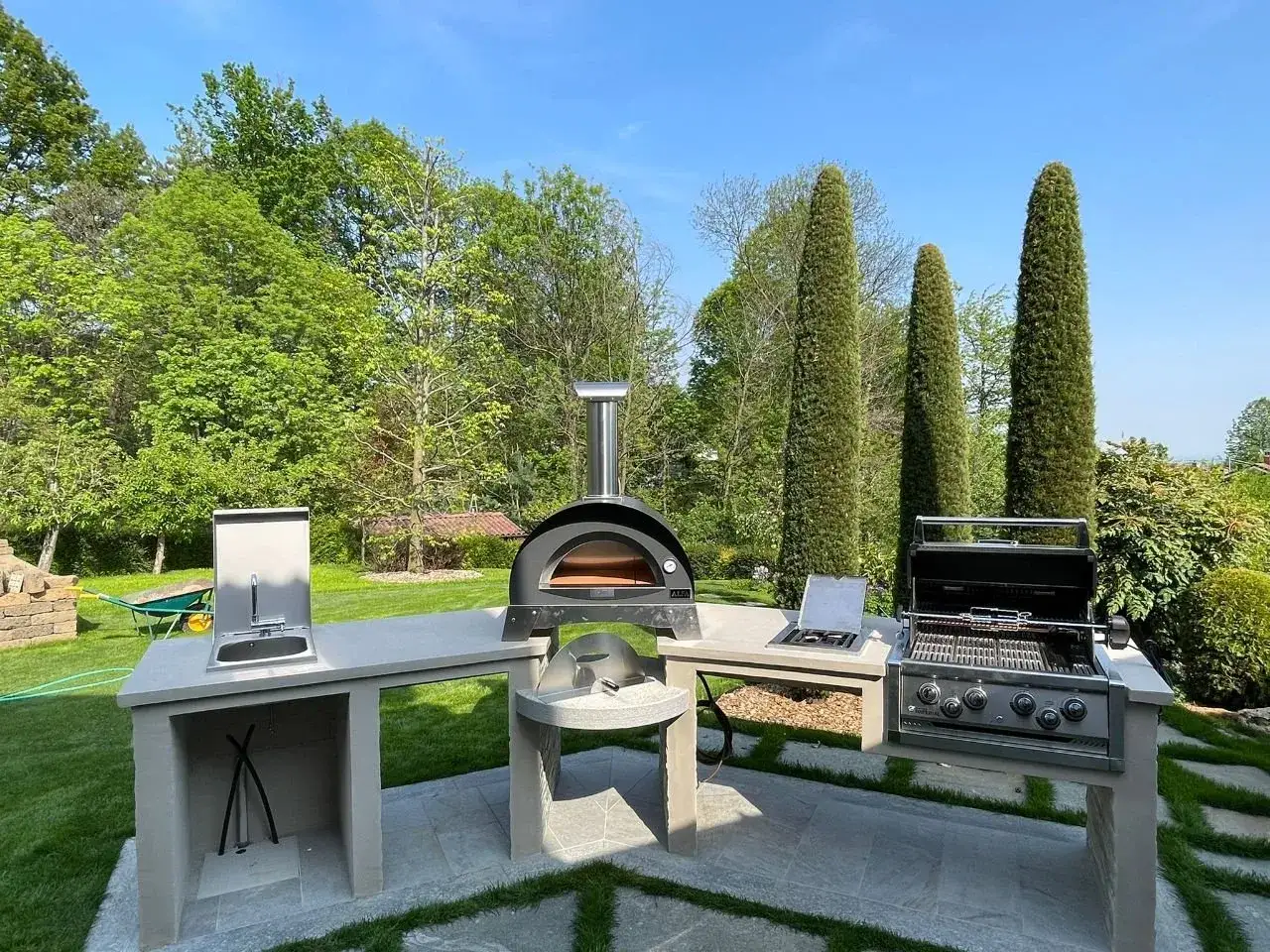 Cucina esterna in muratura fai da te con forno a legna, barbecue e lavello, pronta per grigliate e pizze sotto il sole.