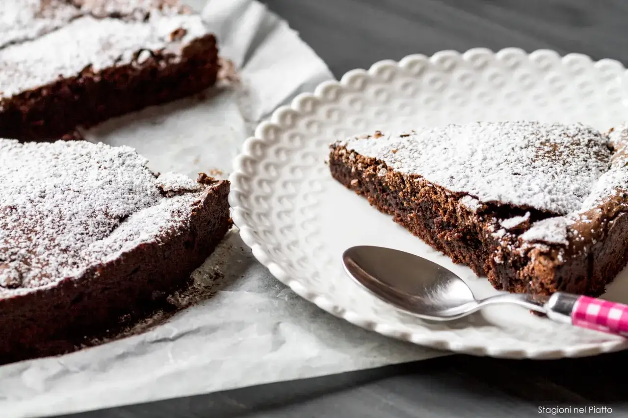 Fette di torta al cioccolato al latte, spolverate di zucchero a velo, su un piatto bianco con un cucchiaino.
