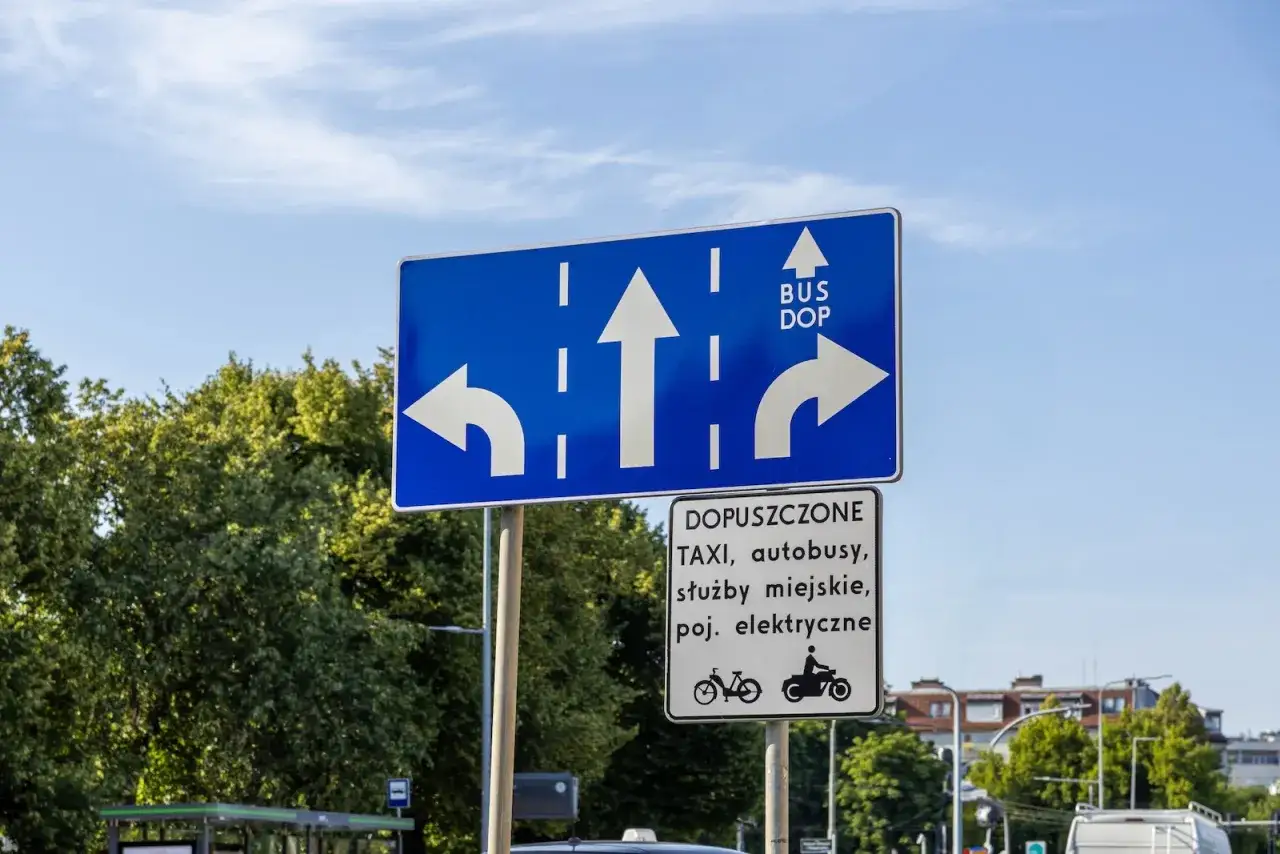 Niebieski znak drogowy z białymi strzałkami: w lewo, prosto, w prawo. Obok strzałki w prawo napis