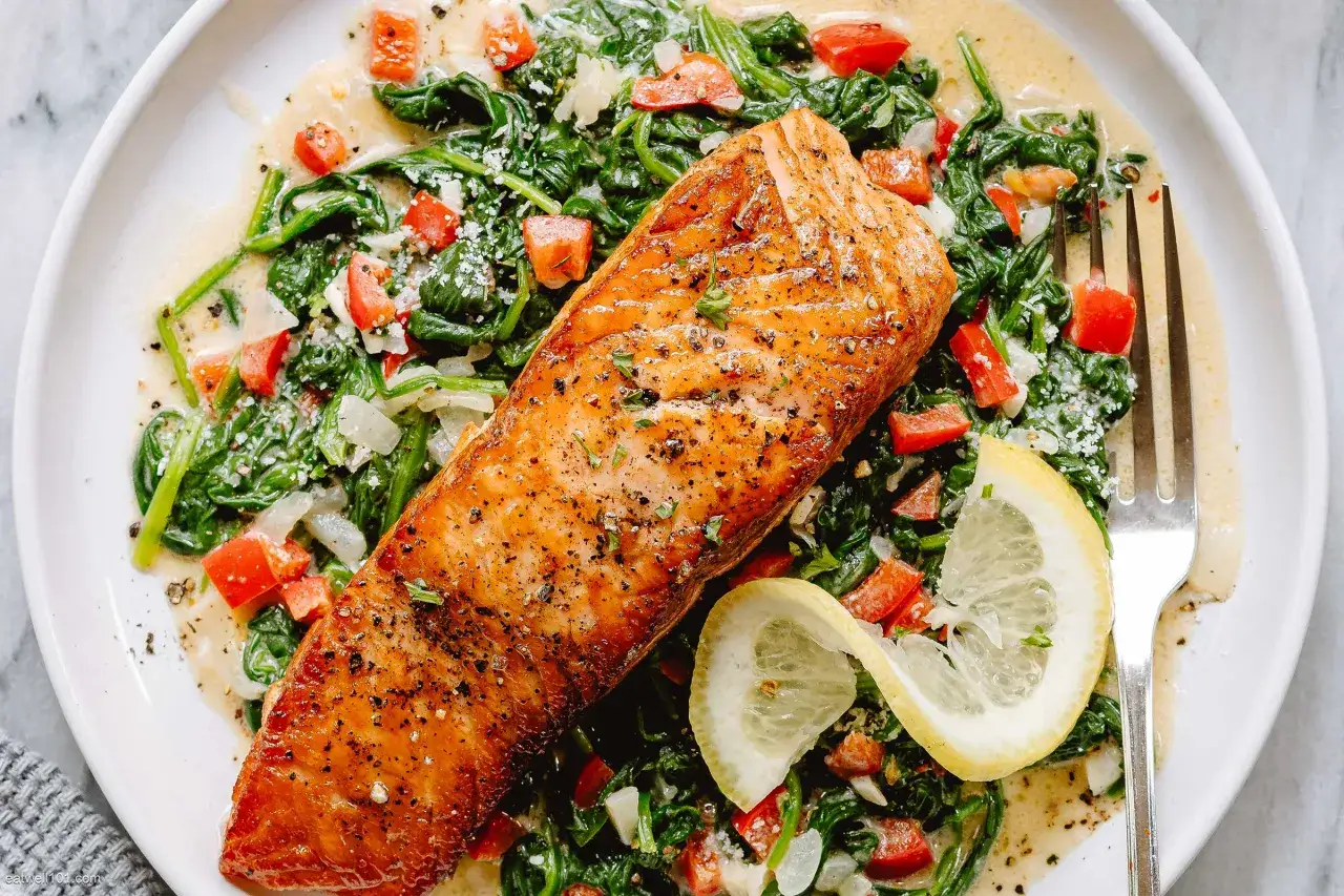 Ein saftiges Stück Lachs mit Spinat und Tomaten, garniert mit Zitronenspalten.