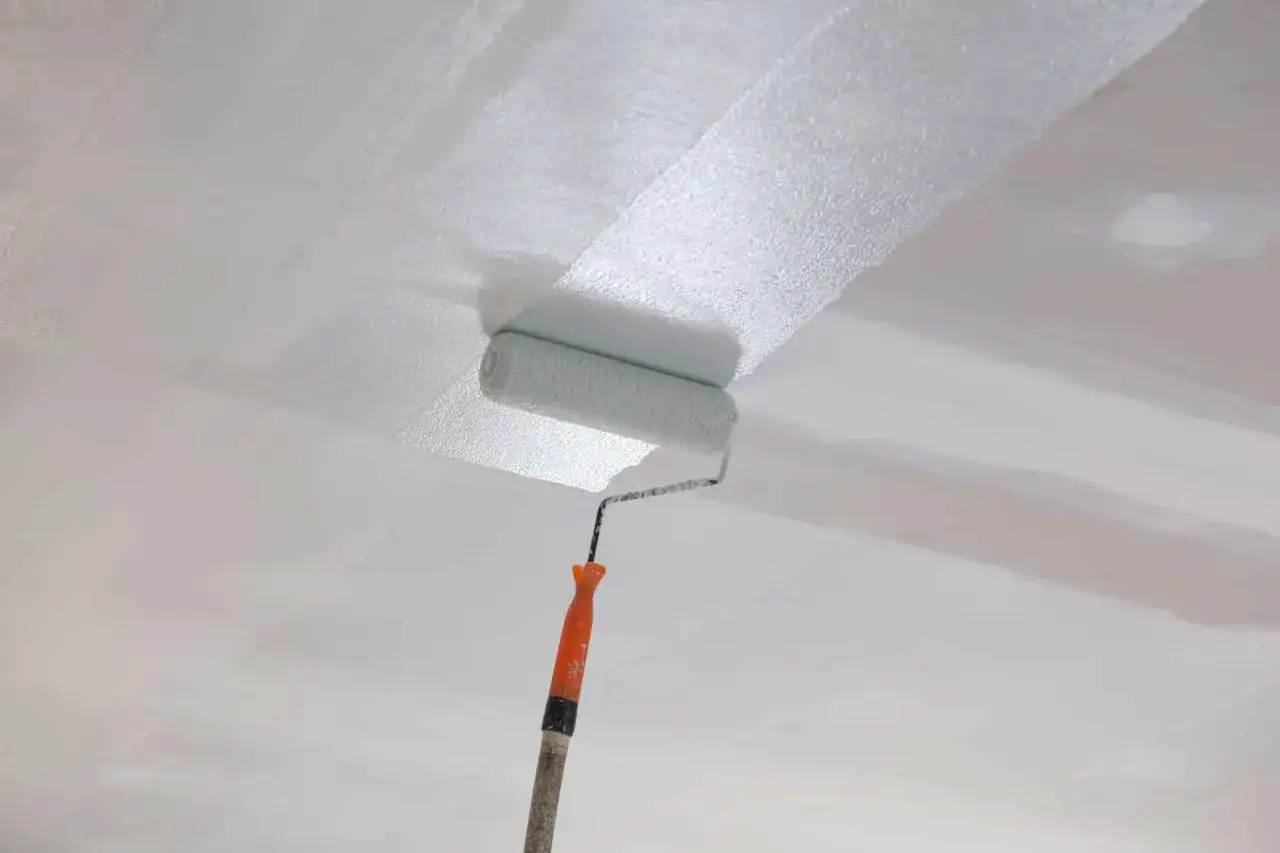 Application d'un enduit mur intérieur au rouleau, créant une surface lisse et prête à peindre.