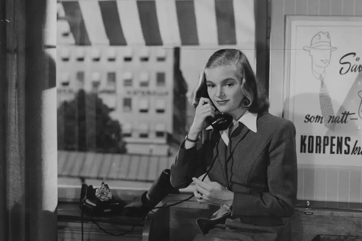 Eva Henning pratar i telefon vid ett fönster med utsikt över en stad.