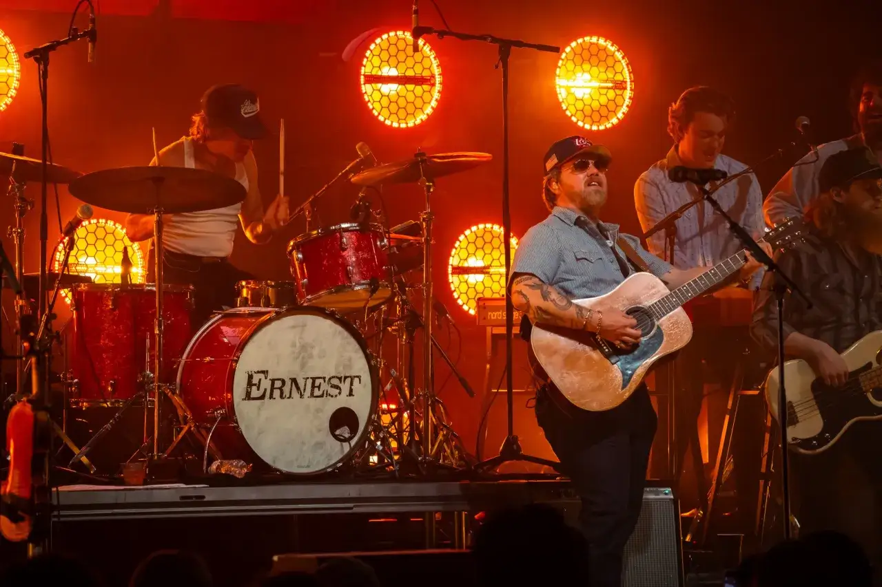 Ernest Keith Smith plays guitar on stage with his band, bathed in warm orange light.