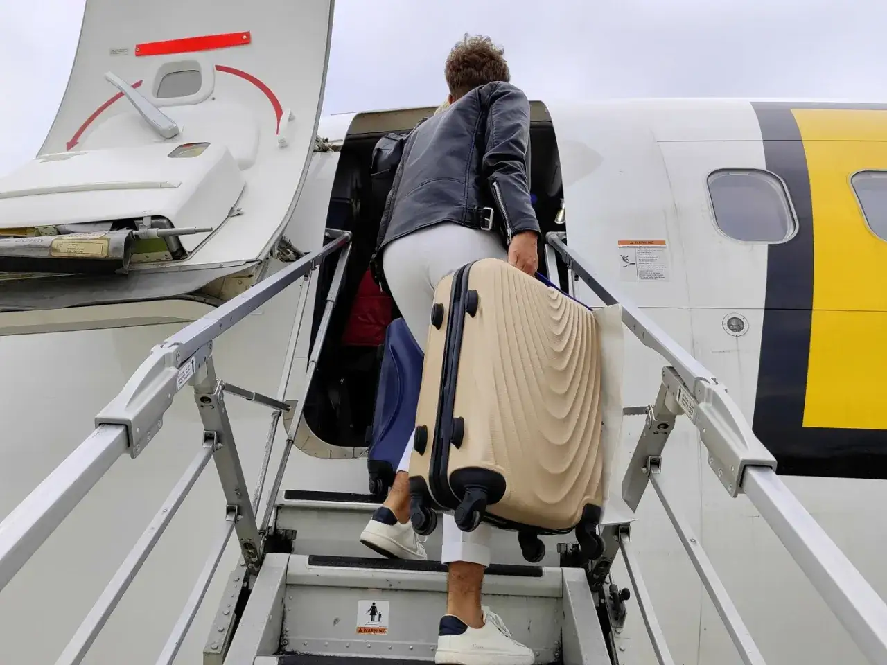 Osoba z bagażem podręcznym Pegasus Airlines wchodzi po schodach do samolotu.
