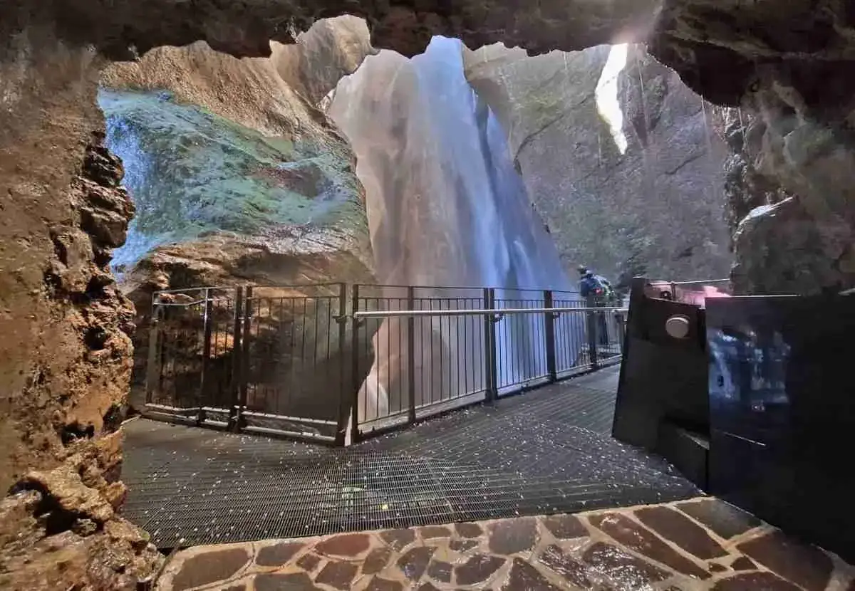 Vue depuis une grotte sur la cascade du Varone, avec une passerelle et une personne admirant le spectacle.