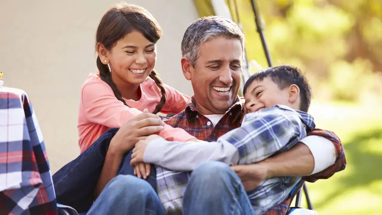 Padre riendo con sus hijos. Un abrazo familiar que puede ser parte del tratamiento para la ansiedad en niños de 5 a 12 años.
