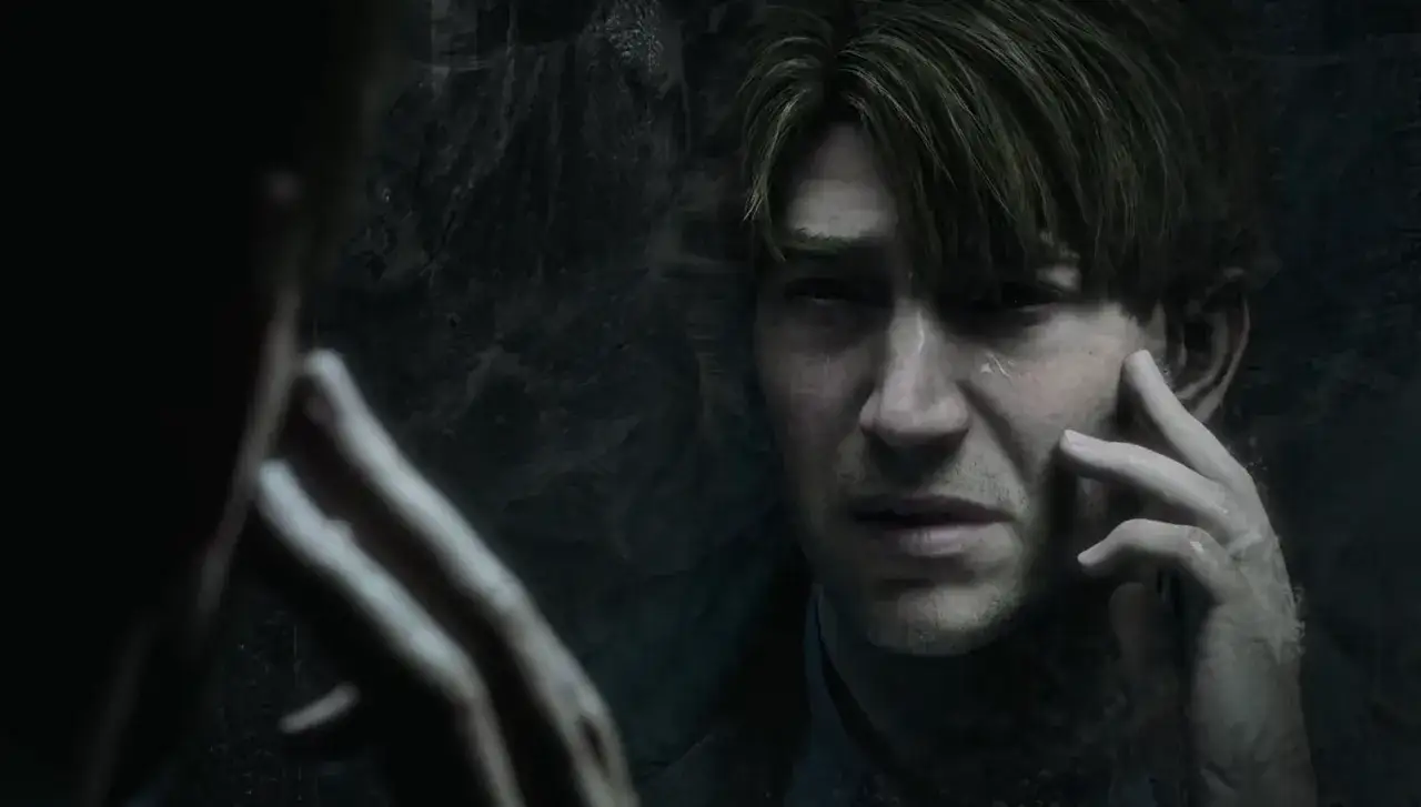 James Sunderland z Silent Hill 2, zamyślony, dotyka swojej twarzy, odbijając się w zamazanym lustrze.