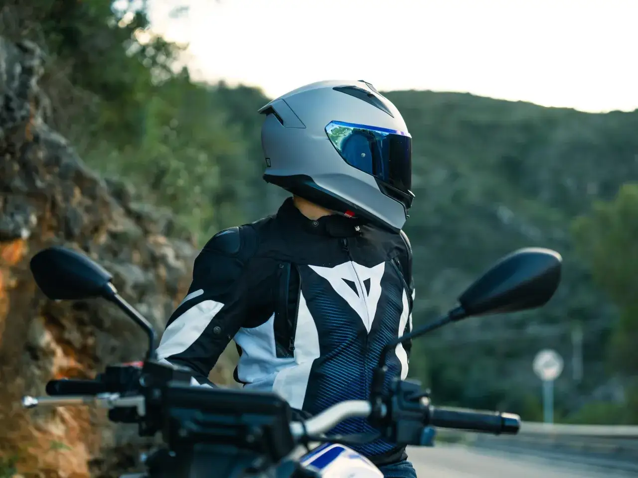 Motorcyklist i en snygg Dainese skinnjacka med vit logga, redo f&ouml;r en tur p&aring; v&auml;gen.