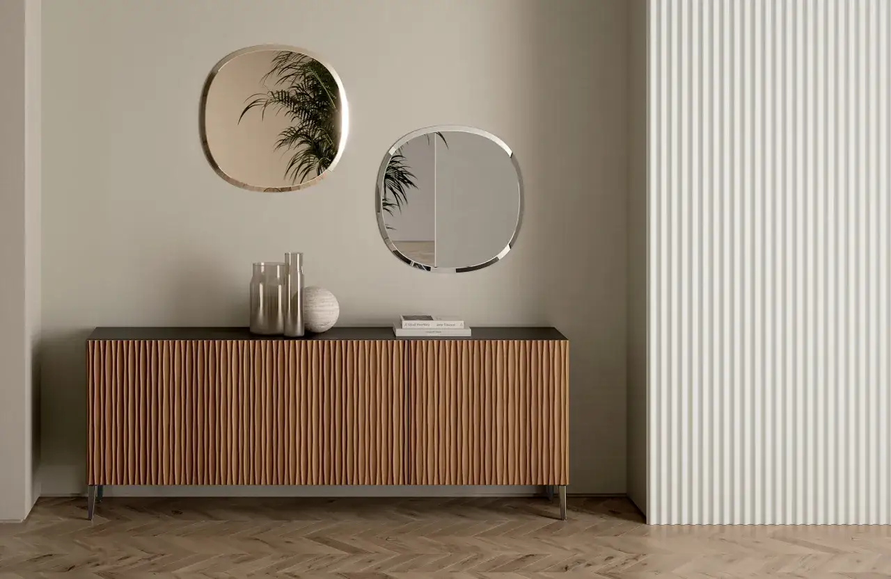 Una madia moderna con ante a listelli in legno, decorata con vasi e libri, sotto due specchi ovali.