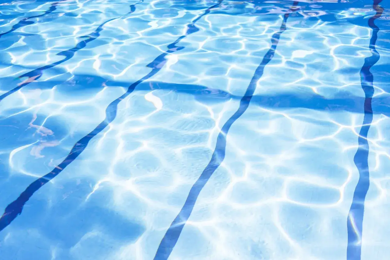 Sunlight dances on the clear blue water of a swimming pool, highlighting the lane lines. This image is perfect for illustrating how to shock a pool for a sparkling clean swim.