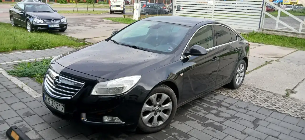 Czarny Opel z rejestracją WLS 35217 zaparkowany na kostce brukowej.