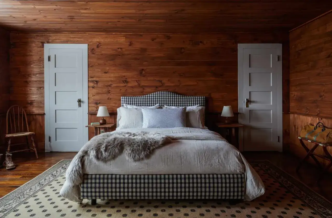 Acogedora habitación de madera con cama a cuadros, ideal para saber como dormir plácidamente. Alfombra y detalles rústicos.