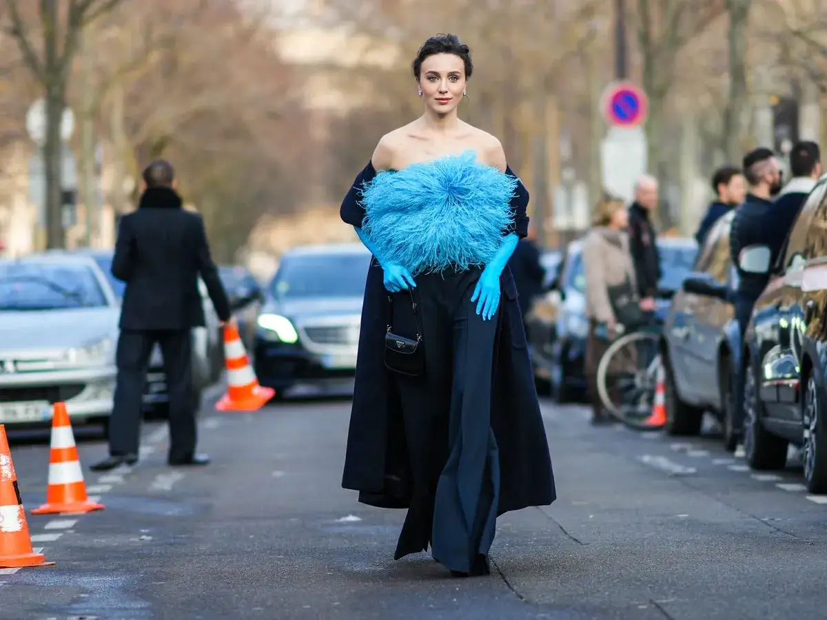 A woman walks down a street in a dramatic blue feathered top and matching opera gloves, showcasing the opera gloves trend.