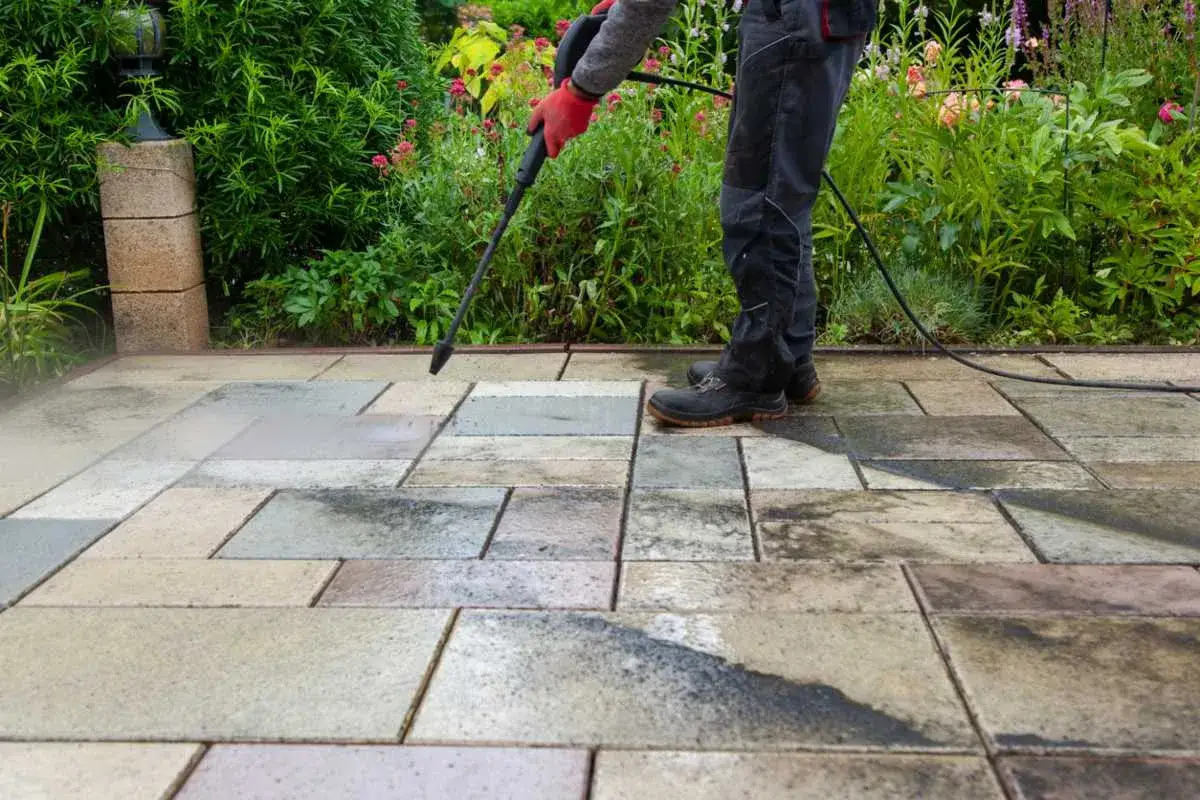 Persona con guantes rojos usa hidrolimpiadora para limpiar suelo terraza de baldosas.
