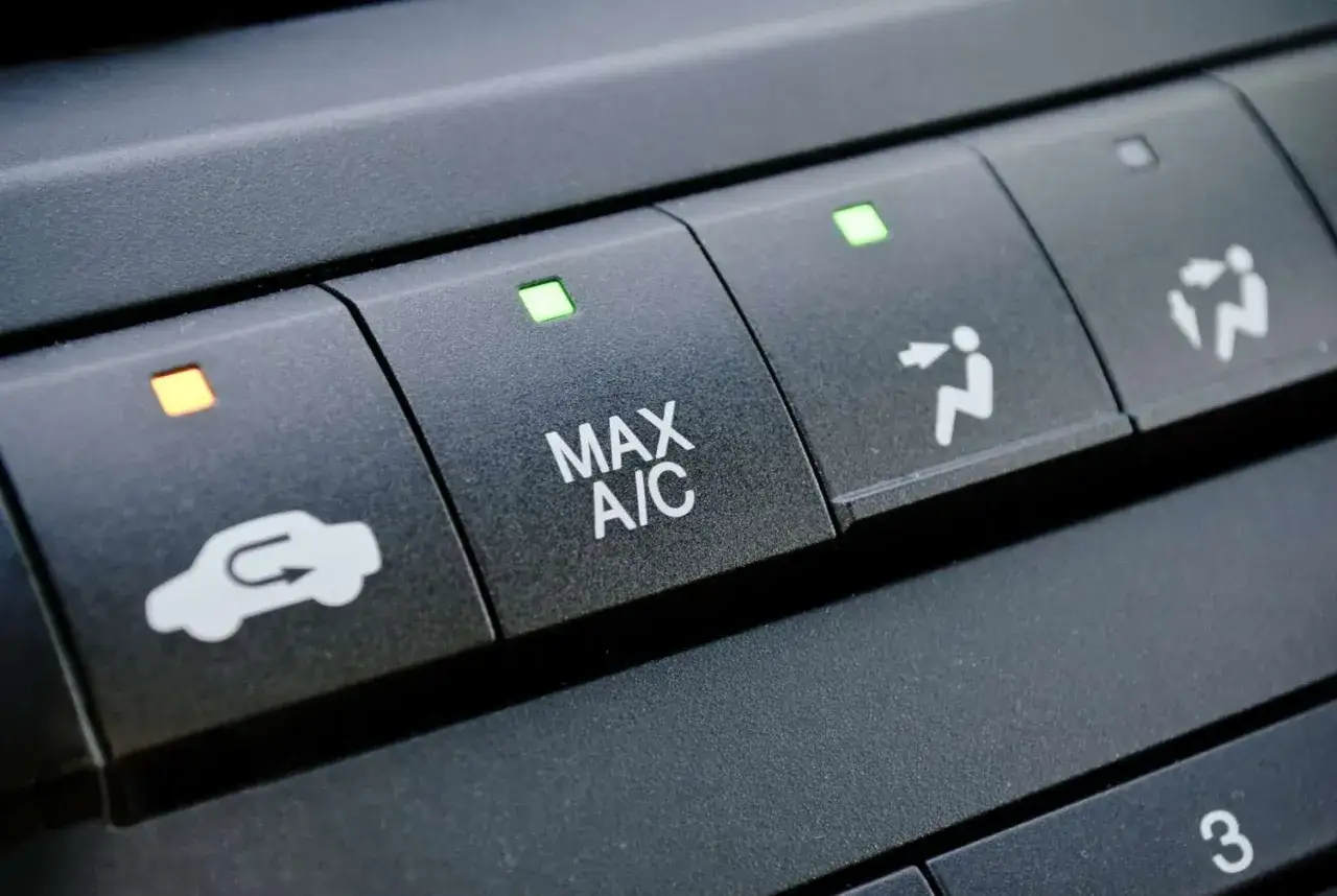 Bot&oacute;n de recirculaci&oacute;n de aire en un coche, junto a MAX A/C y otros controles clim&aacute;ticos.