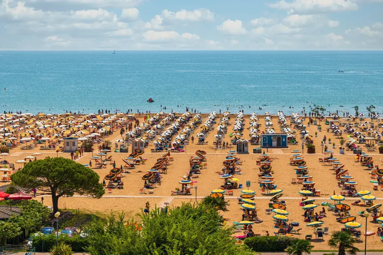 Una spiaggia affollata vicino a Venezia, con file ordinate di ombrelloni gialli e bianchi e persone che si godono il sole e il mare azzurro.