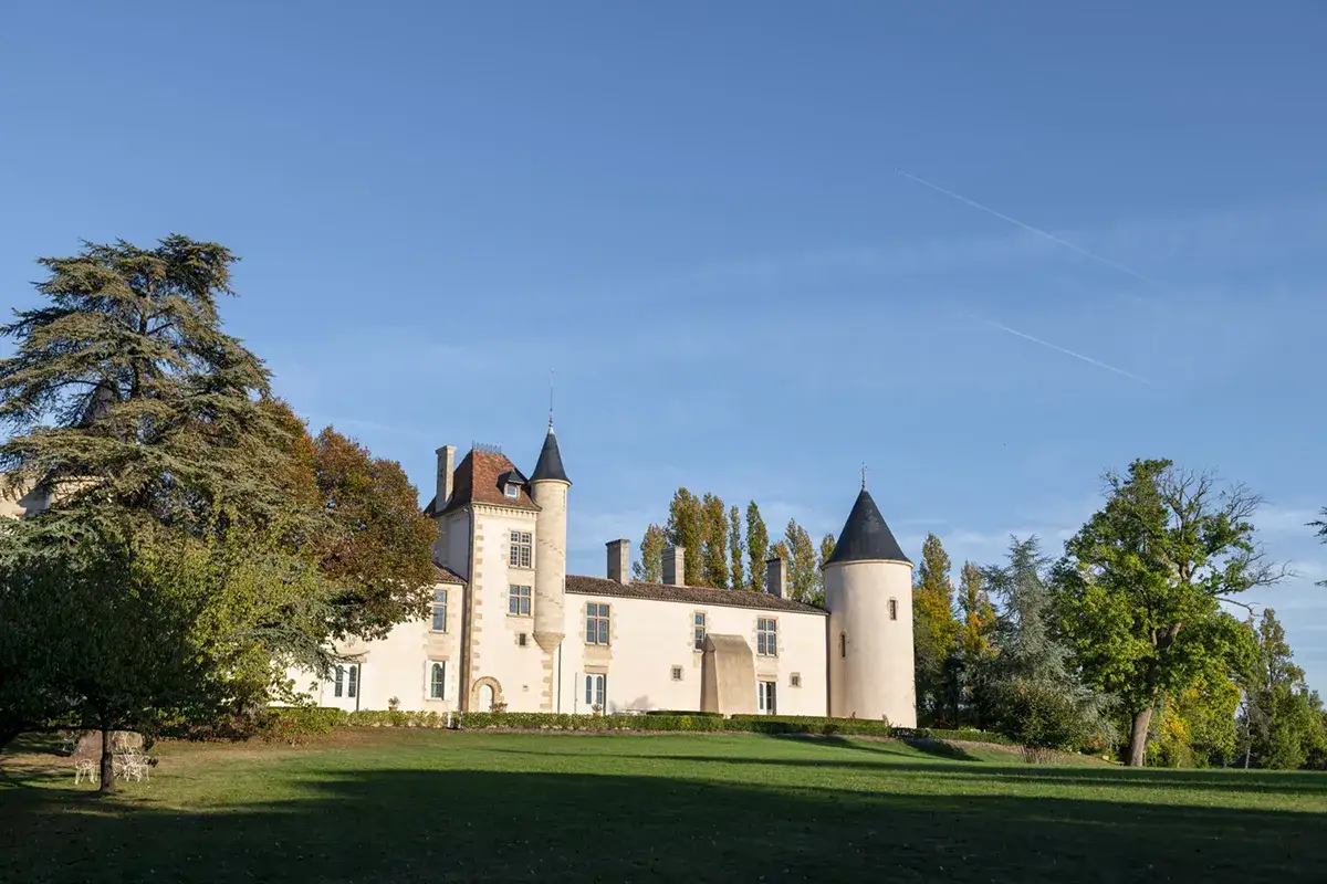 Le château de Toulouse-Lautrec, un édifice de pierre claire avec des tours coniques, se dresse sous un ciel bleu clair, entouré d'arbres aux couleurs d'automne.