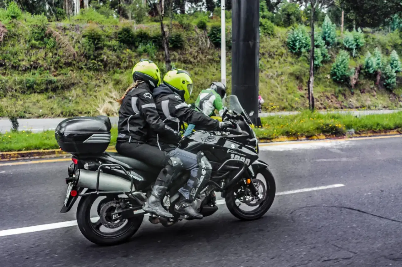 Coppia in moto, la posizione passeggero moto è ben visibile, con caschi gialli e abbigliamento tecnico.