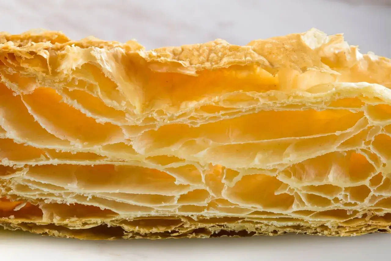 Texture aérienne et dorée d'une pâte feuilletée, révélant ses multiples couches croustillantes et légères.