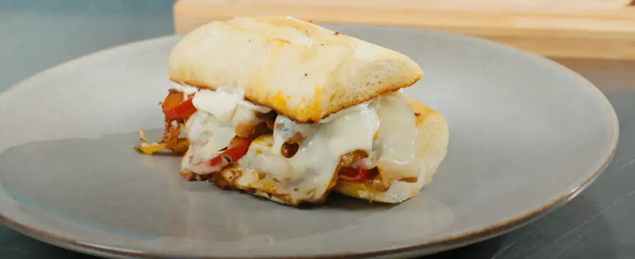 En saftig steak sandwich med sm&auml;lt ost och paprika p&aring; en tallrik.